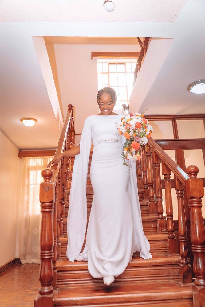 A bride in a white gown descending a wooden staircase