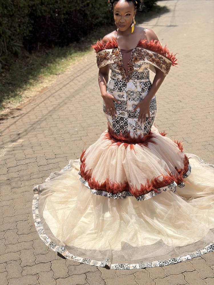 A bride in a traditional custom Beige gown with highlights of burnt orange embellishments and feathers for detail.
